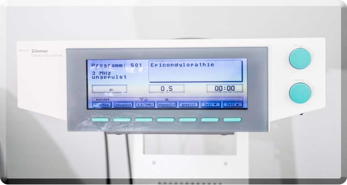 Nahaufnahme des Bildschirms eines medizinischen Ultraschallgeräts 'Sono 5 Zimmer MedizinSysteme'. Der Bildschirm zeigt 'Programm: S01 Epicondylopathie', '3 MHz ungepulst' und die Einstellwerte '0.5' sowie '00:00'.