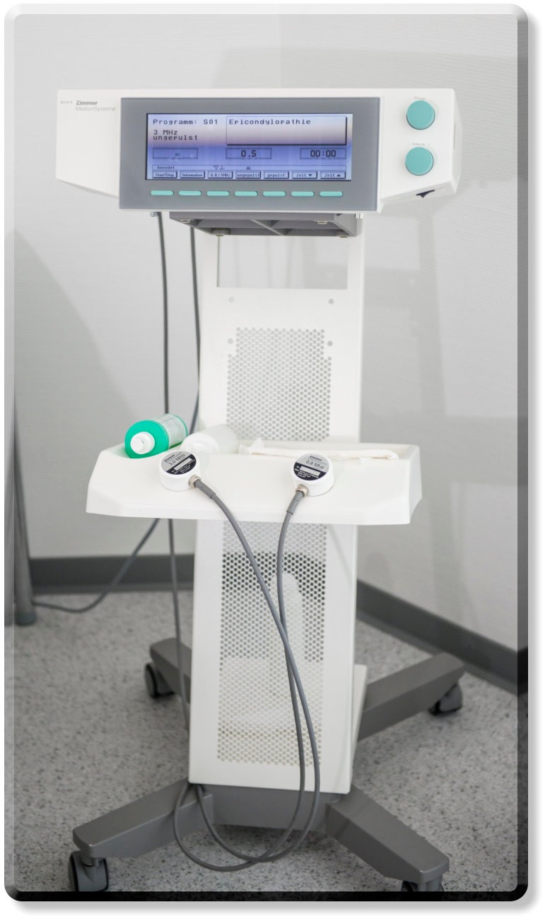 Ein medizinisches Ultraschallgerät 'Sono 5 Zimmer MedizinSysteme' auf einem fahrbaren Ständer. Der Bildschirm oben zeigt Programminformationen an. An der Seite sind zwei grüne Regler und an der Front zwei Schallköpfe angeschlossen.